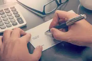 Writing payment cheque at the table with calculator and glasses