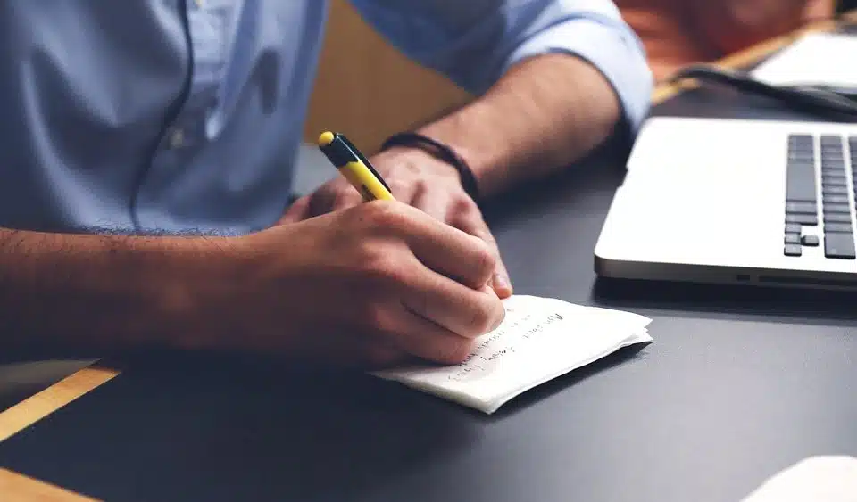 In an office environment, a man in a suit is diligently taking notes at his desk