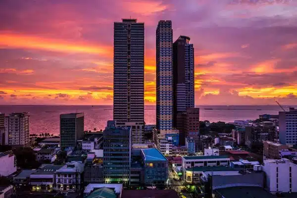 Tall buildings stand silhouetted against the backdrop of a sunset