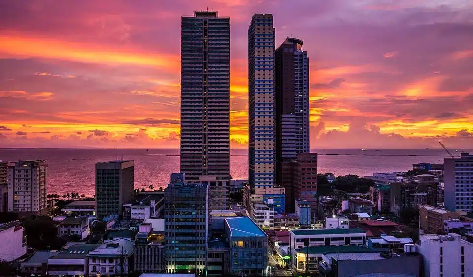 Tall buildings stand silhouetted against the backdrop of a sunset