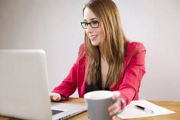 A woman in pink smiling in front of her laptop, holding a mug