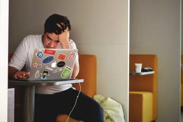 The man is seated, his expression focused as he looks at his laptop screen.