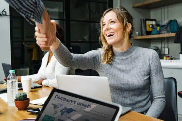 A woman smiles as she shakes hands with someone in an office setting.